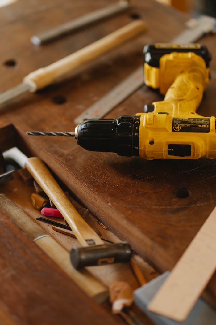 About From above of contemporary screwdriver with drill near hammer and tools on wooden desk