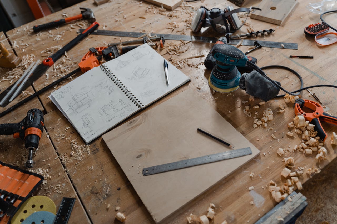Home A detailed view of woodworking tools and sketches on a workshop table, showcasing the craft of carpentry.